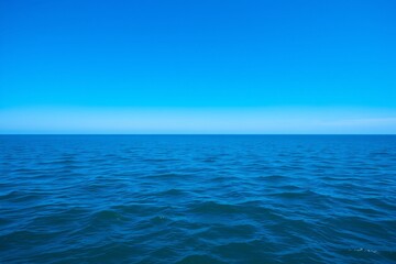 Fototapeta premium Tranquil view of an endless blue ocean meeting the bright, clear sky, conveying peace and serenity.