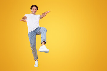 Having Fun. Full body length portrait of happy young handsome bearded guy jumping, dancing and looking at camera, being in a good mood, isolated over bright orange background, vertical studio shot