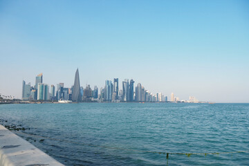 Fototapeta premium Qatar City skyline rises over calm waters during bright sunny day