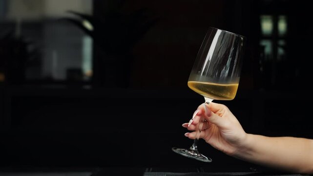 Close-up shot of a woman's hand holding a wine glass. The girl is holding a glass of white wine in her hands. A glass of wine in the hands of a taster.
