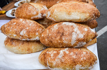 Stacks of freshly baked artisan bread with a golden crust displayed on a market stall. Perfectly capturing the essence of traditional and natural baking craft