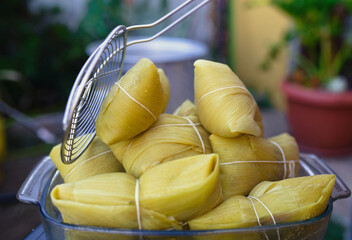 Photographs of a person preparing humitas using choclos, corn on the cob and a person eating humitas in a house in Chile