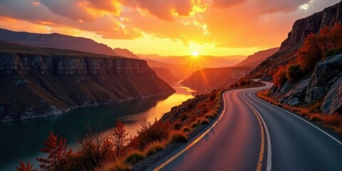 Fototapeta premium A scenic highway curves gracefully along a canyon's edge, bathed in the warm glow of a breathtaking sunset, reflecting upon a tranquil body of water nestled amidst majestic mountain peaks.