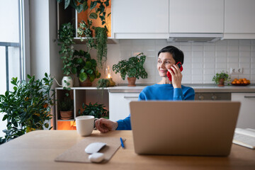Smiling relaxed mature woman talking on smartphone, consulting clients while drinking tea in...