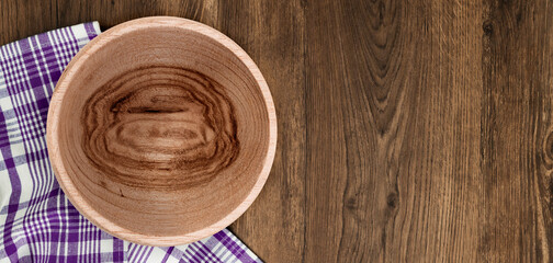 Handcrafted wooden bowl with natural grain texture on rustic wooden table with purple checkered napkin, ideal for eco-friendly dining and kitchen decor.