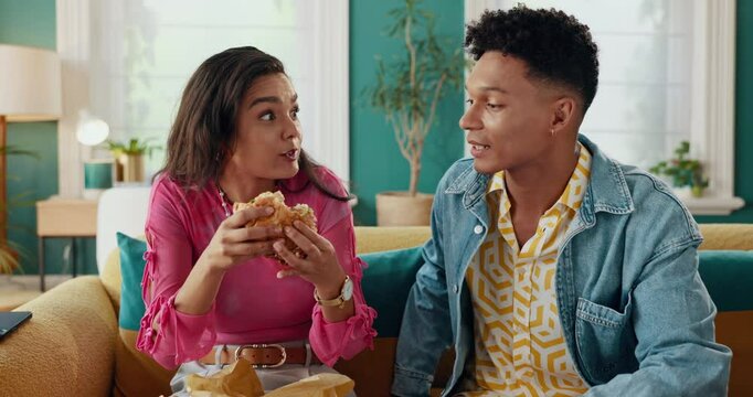Fast food, eating and burger with couple on sofa for takeaway, nutrition and dinner date. Feeding, happiness and hungry with man and woman in living room at home for sandwich meal, cuisine and relax