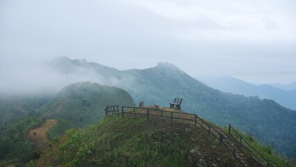 Wooden chair and fence on the mountain peak on foggy morning