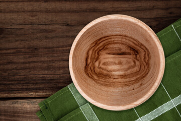 Handcrafted wooden bowl with natural grain texture on rustic wooden table with green napkin.