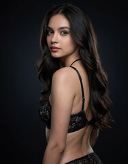 Fototapeta premium Elegant woman with long wavy hair wearing black lace lingerie posing against dark background, confident and sensual expression, studio lighting
