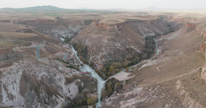 Drone moves towards historical rock settlements in Kayseri Soğanlı Valley. Natural rock formations and carved structures bear traces of ancient settlements spread across the valley.