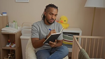 Man writing in notebook while seated in baby's room with crib and yellow duck plush in the background, showcasing a thoughtful moment in a serene and organized home environment.