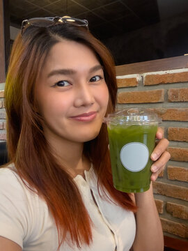 Vertical photo, asian Thai woman selfie while hlding ice pure matcha green tea, relaxing in cafe.
