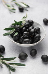 Black olives with olive branches served in ceramic bowl on gray background