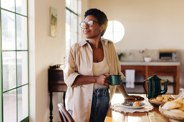 Thoughtful black woman enjoying her morning with fresh coffee and cheese bread rolls