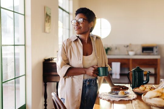 Thoughtful black woman enjoying her morning with fresh coffee and cheese bread rolls