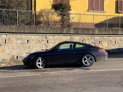 Black Porsche 996 Carrera 4 parked near a stone wall