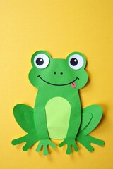 Obraz premium A Cheerful Green Paper Frog with Big Eyes and a Happy Expression on a Yellow Background