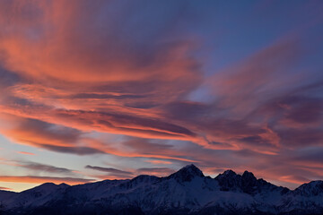 Colorful pink clouds at sunrise over rugged Alaska mountain range.