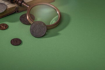 Numismatics. Ancient collectible coins and magnifying glass on a green table.