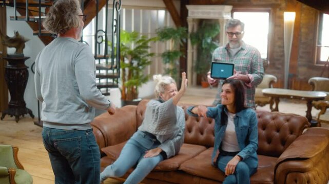 Group of retired friends playing word games using a digital tablet during a social gathering at home. Elderly man showing pantomime gesticulating forms explaining play guessing games using app game.