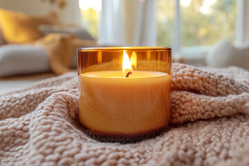 Burning candle in amber glass on a soft knit blanket, radiating warm glow, peaceful atmosphere, and cozy vibes, perfect for autumn and winter home decor scenes.