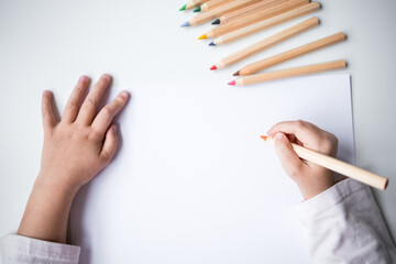 Childs hands drawing with colored pencils on white paper