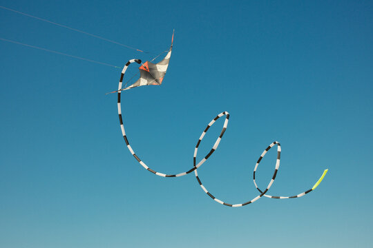 Kite flying high in the clear blue sky with long checkered tail