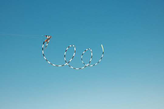 Kite flying high in the clear blue sky with long checkered tail