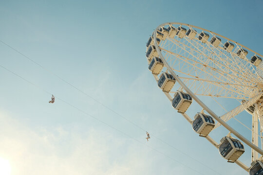 Tourists ziplining over ferris wheel on sunny day