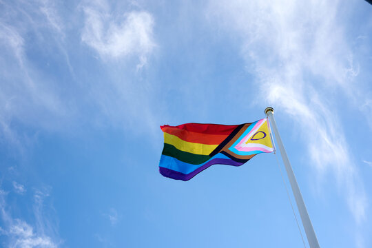Progress pride flag waving in the wind against a blue sky