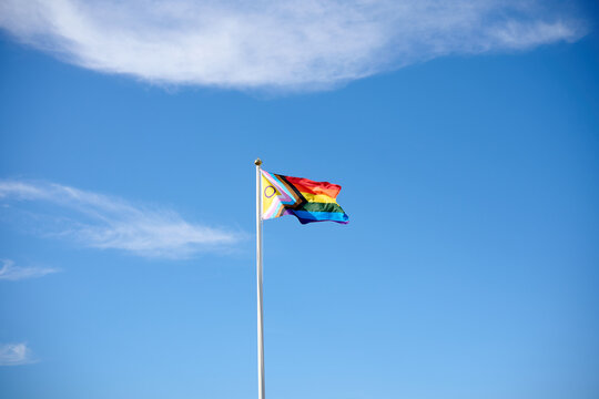 Progress pride flag waving on flagpole with blue sky background