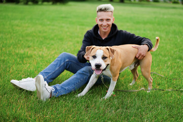 Man and dog in the park. Happy man embracing a young american bulldog. Young caucasian man hugging his dog in nature. caucasian.
