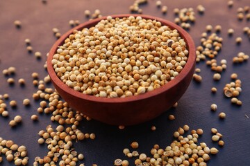 Coriander or Coriandrum sativum in a wooden bowl and some scattered around it, with black background and close up view.