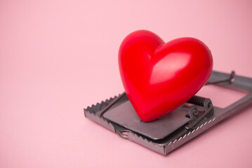 Red heart in a rat trap on pink background. Online internet romance scam or valentine day in darkside concept. Love is bait or victim.