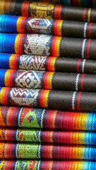 Vertical image of Close up of brightly colored folded traditional fabric for sale at Otavalo market in Ecuador