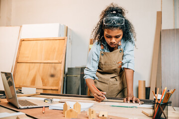 African American carpenter woman drawing a line on wood with a pencil and ruler in workshop. Focused on precise measurements, woodworking, and construction tasks in carpentry, National Carpenters Day