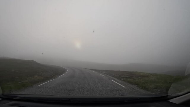 Driving on the E69 road through the tundra in northern Norway. Misty hills covered with grass and scattered stones surround the route, creating a remote and atmospheric landscape.