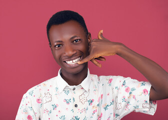 A young man in a floral shirt playfully mimics talking on an imaginary phone with his hand against...