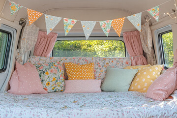 Cozy and inviting camper van interior with floral and pastel decor, featuring bunting, cushions, and curtains, creating a serene and charming atmosphere for relaxation.
