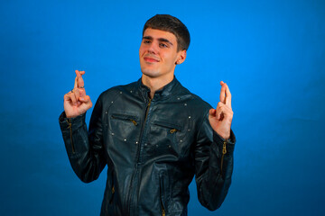 Young man crossing fingers hoping for good luck on blue background