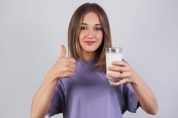 Fototapeta premium Portrait of a satisfied young woman in a purple t-shirt drinking milk from the glass isolated over light background