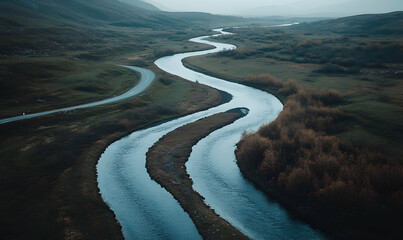 Fototapeta premium Serpentine river meandering through a tranquil landscape, alongside a winding road. Aerial view showcasing nature's beauty.