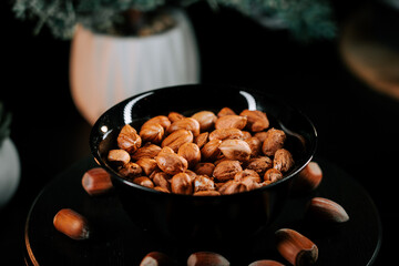 Hazelnuts in a black bowl on a dark surface surrounded by additional nuts creating an elegant and inviting display