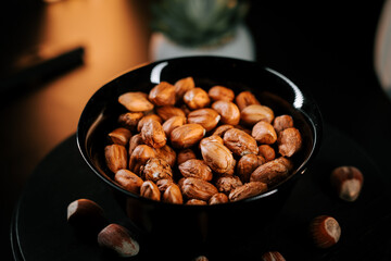 Hazelnuts arranged in a black bowl on a dark background, highlighting their natural texture and...