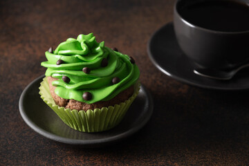 St. Patrick's Day coffee and homemade cupcake with green whipped cream and chocolate sprinkles on brown background. Close up. Festive food,