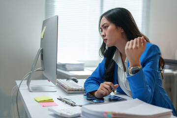 Young asian businesswoman looking concerned at computer screen while working in office with...