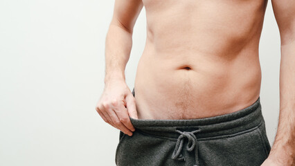 Naklejka premium Man showing weight loss by showing his loose pants. Fit young man pinching his stomach