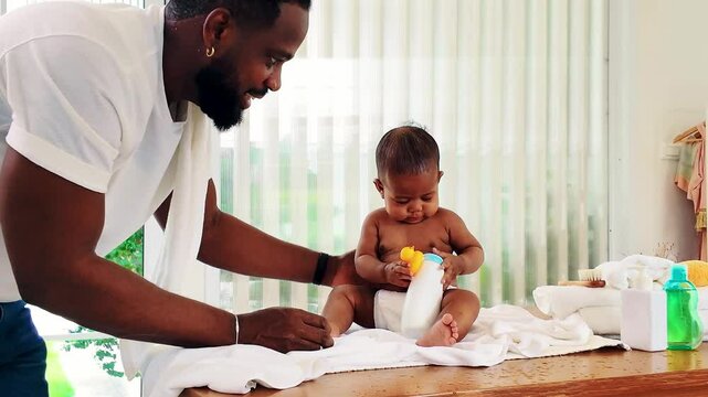 Caring Black father changes his baby&rsquo;s diaper while the infant cries, capturing a relatable parenting moment. Fatherhood, baby care, and everyday parenting struggles in a bright home setting. 4k video