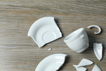 White cup and plate broken on wooden background