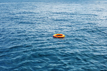Orange life buoy float in vast expanse of blue sea. Red lifebuoy drift on ocean waves, selective...